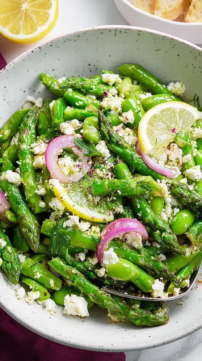 Fresh green asparagus salad with lemon vinaigrette, crumbled feta cheese, and toasted pine nuts on a white platter.
