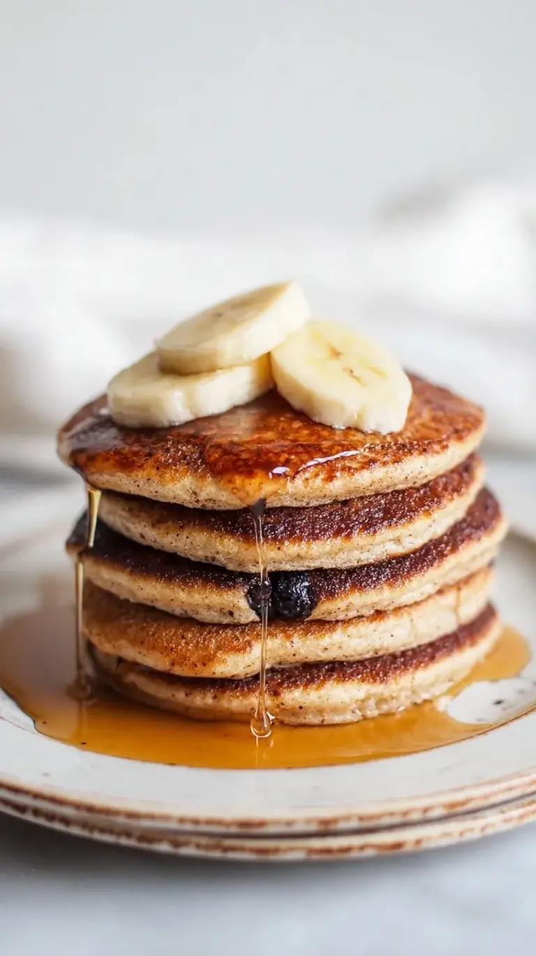 A stack of golden brown banana cottage cheese pancakes topped with sliced bananas and maple syrup