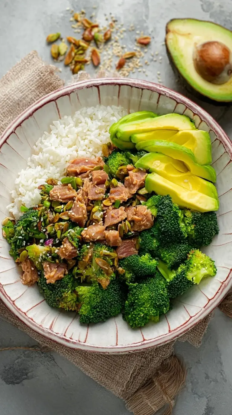 A vibrant Broccoli Avocado Tuna Bowl with steamed green broccoli, flaked tuna, and sliced avocado topped with red chili flakes.
