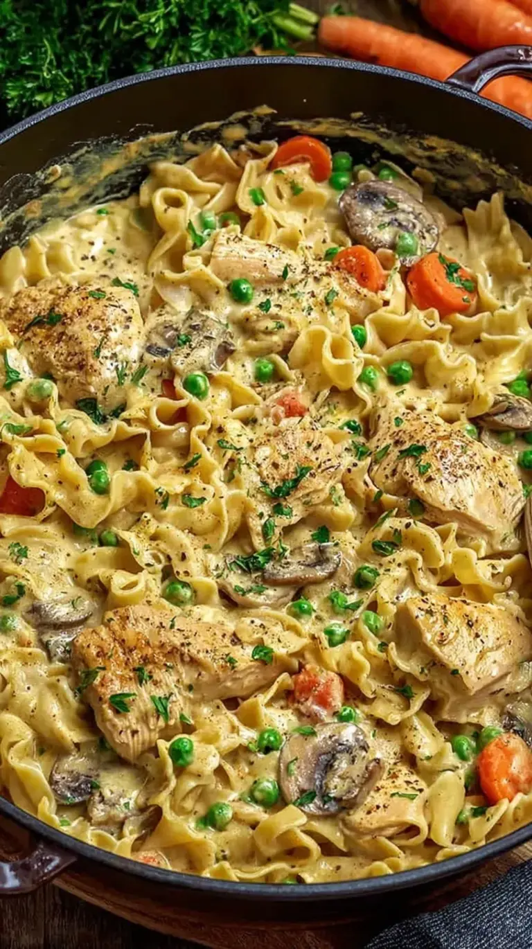 A close-up shot of creamy Chicken Pot Pie Pasta with rotini, chicken, carrots, and peas in a rich white sauce.