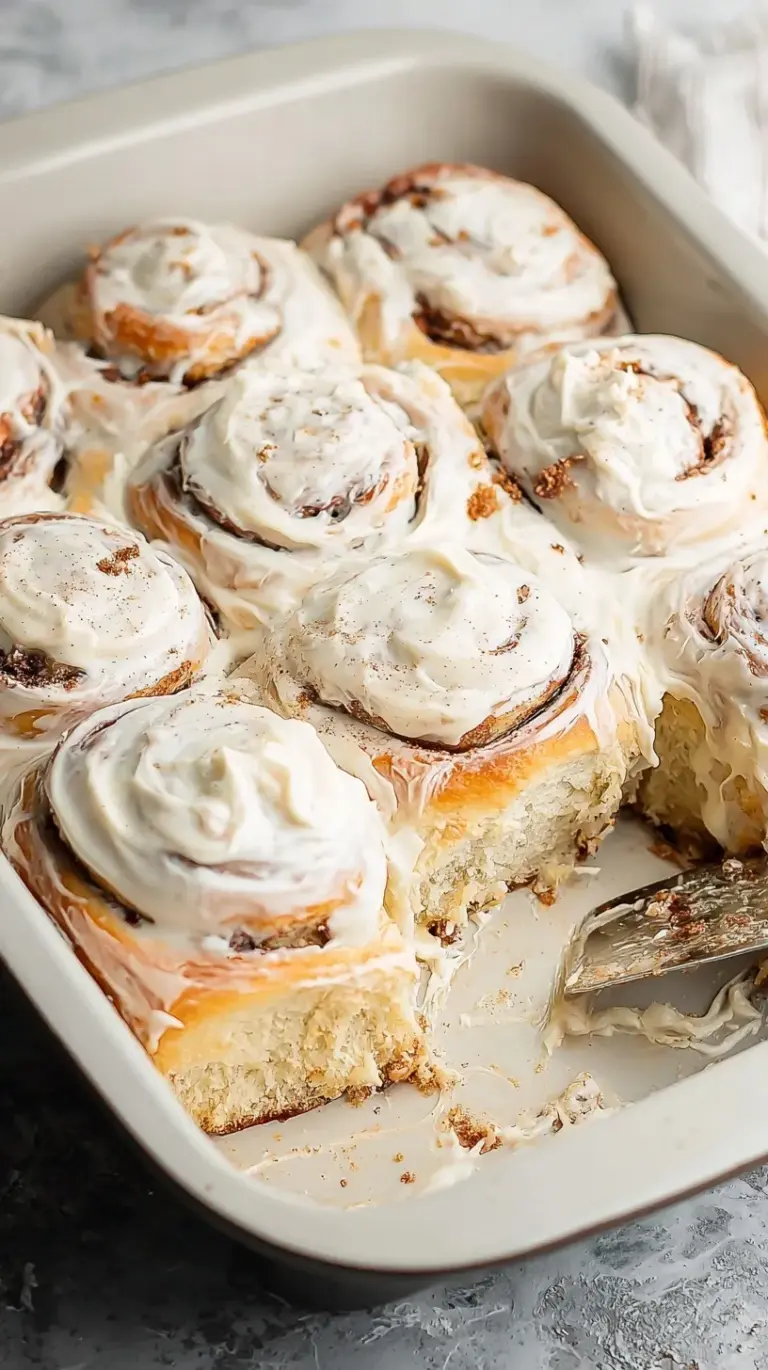 A tray of freshly baked gluten-free cinnamon rolls topped with melting cream cheese frosting.