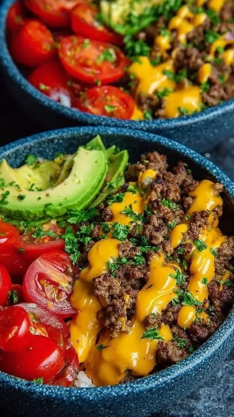 A vibrant cheeseburger bowl with seasoned ground beef, melted cheddar, fresh tomatoes, and creamy sauce over romaine lettuce.