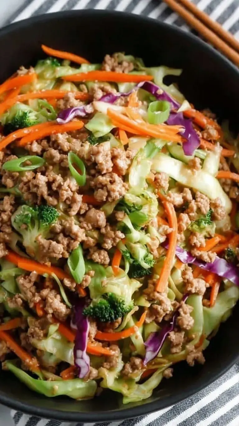 A steaming bowl of ground turkey and shredded cabbage with green onion garnish and sriracha drizzle.