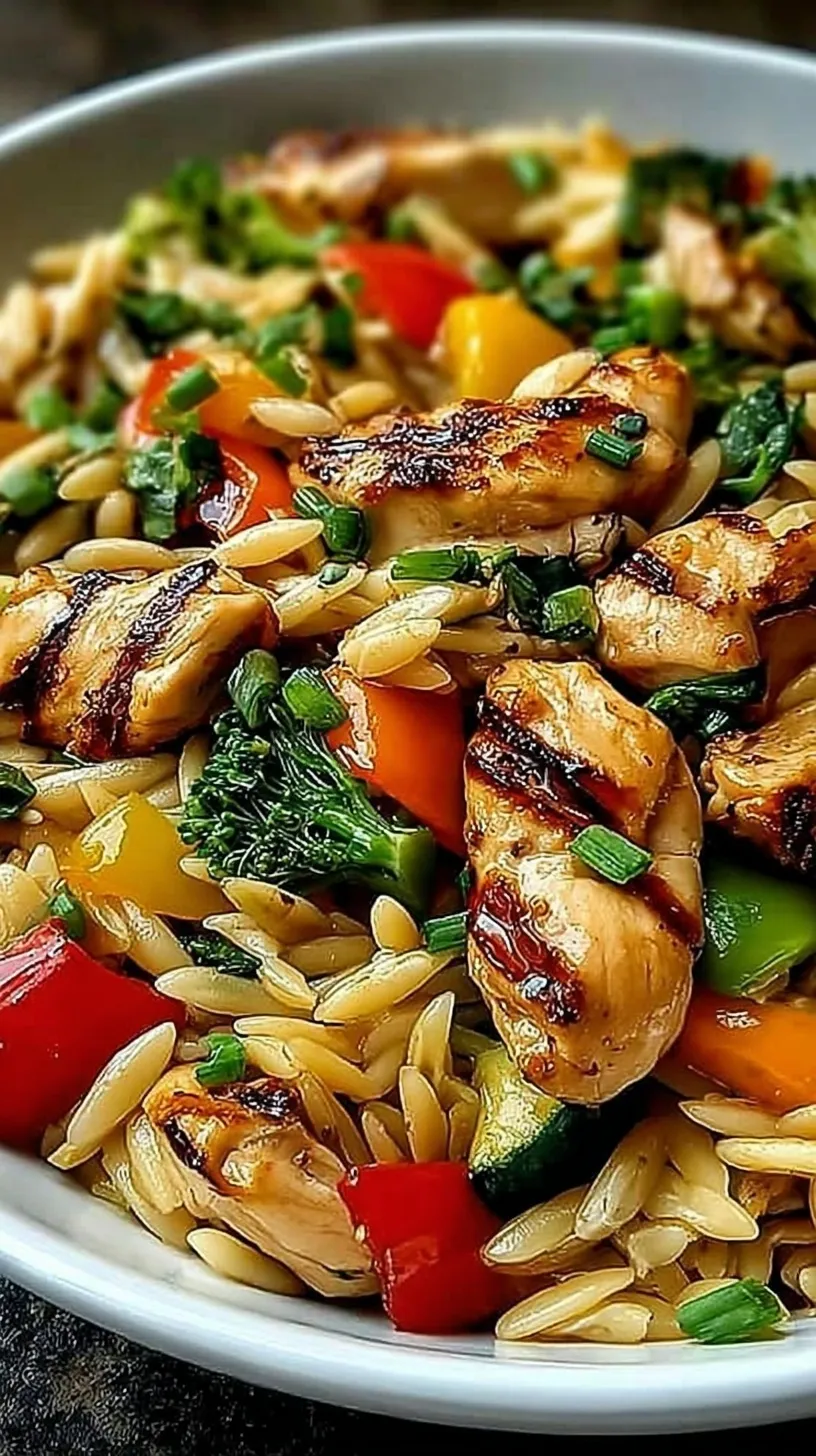 A vibrant skillet of lemon chicken cubes, green zucchini, red peppers, and orzo pasta garnished with fresh parsley.