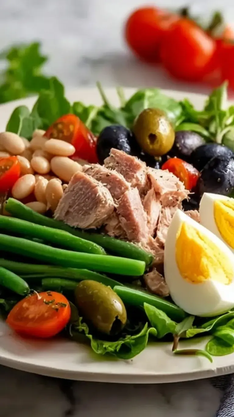 A vibrant Nicoise-style tuna salad with white beans, olives, and cherry tomatoes served on a bed of fresh arugula.