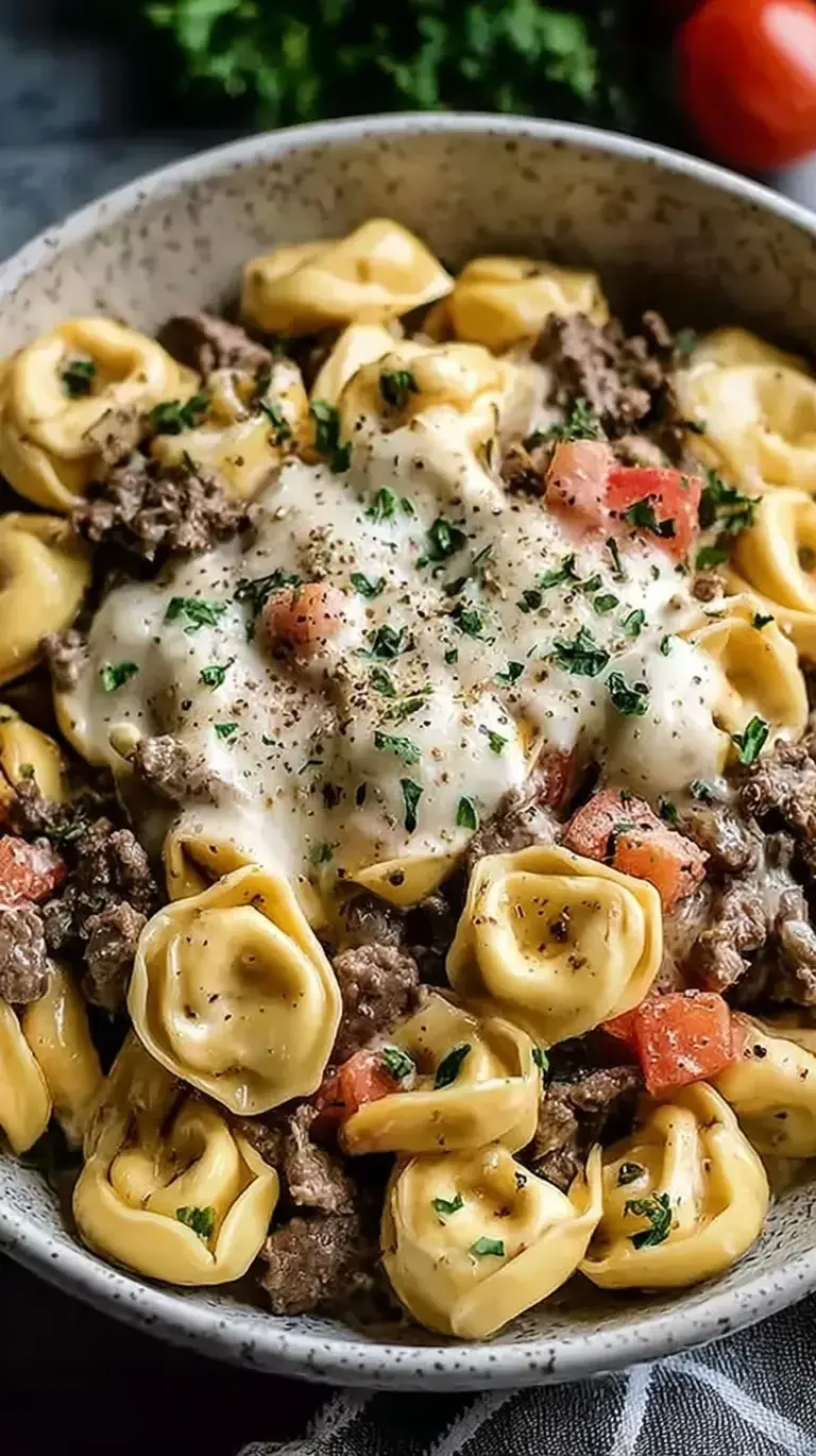 A skillet filled with creamy Philly Cheesesteak Tortellini featuring thinly sliced steak and green peppers.