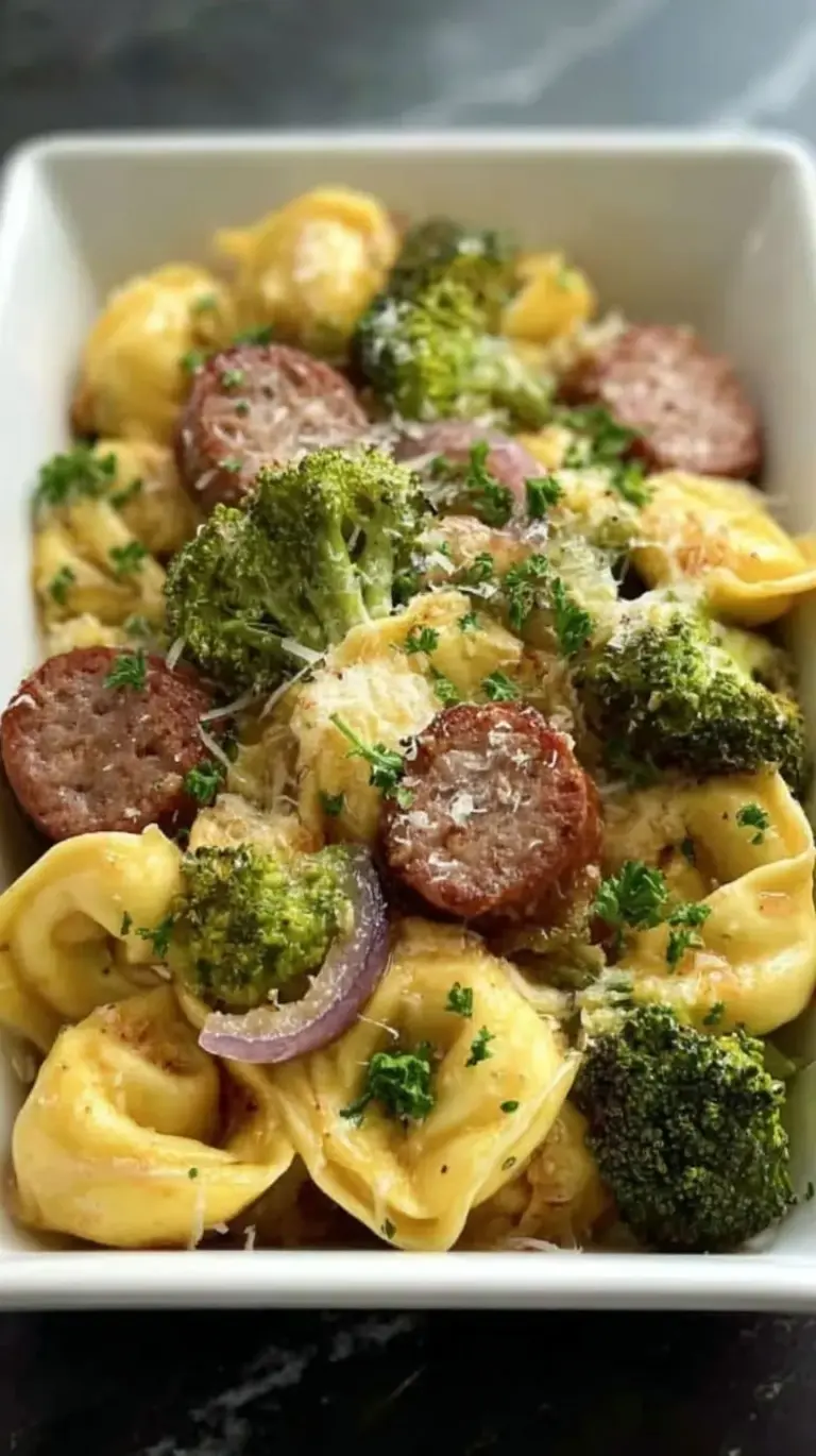 A golden sheet pan filled with roasted cheese tortellini, sliced Italian sausage, zucchini, and cherry tomatoes.