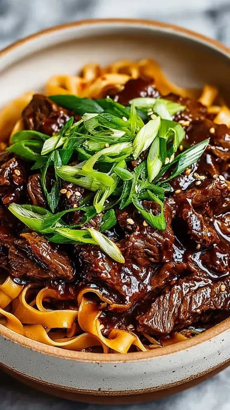A bowl of saucy Slow Cooker Korean Beef Noodles topped with green onions and sesame seeds.