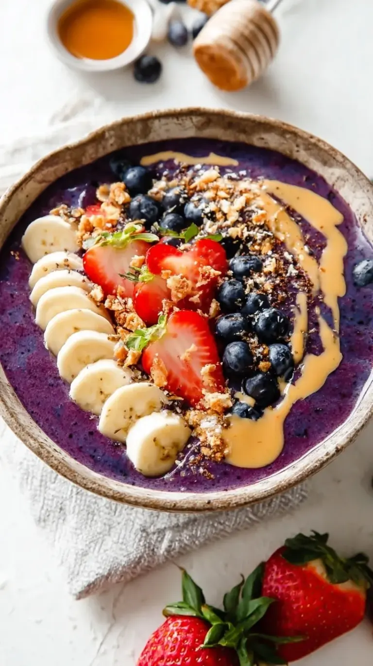 A vibrant purple acai smoothie bowl topped with fresh strawberries, banana, and granola in neat rows.